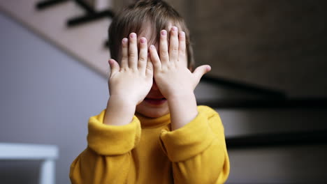 Lovely toddler covering his face with hands. Adorable baby boy opens face smiling sweetly. Close up.