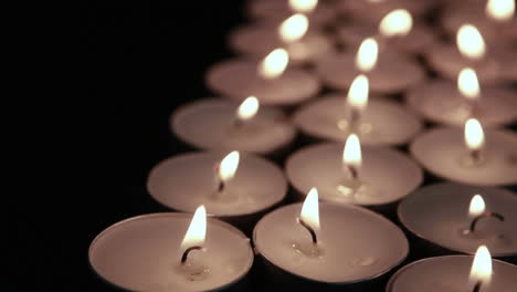 animation of white and yellow zigzag lines over lit tea light candles on black background