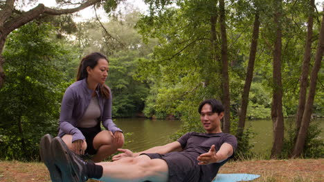 woman teaching man wearing sports clothing in outdoor yoga class surrounded by forest and lake or river 1