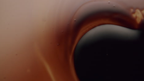 macro shot of a black viscous liquid spreading over another amber liquid