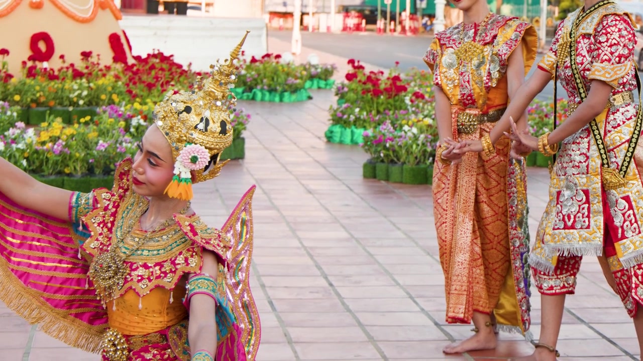 Penampil dengan kostum emas berornamen dan topeng menampilkan gerakan tari klasik Thailand di luar ruangan di Bangkok.