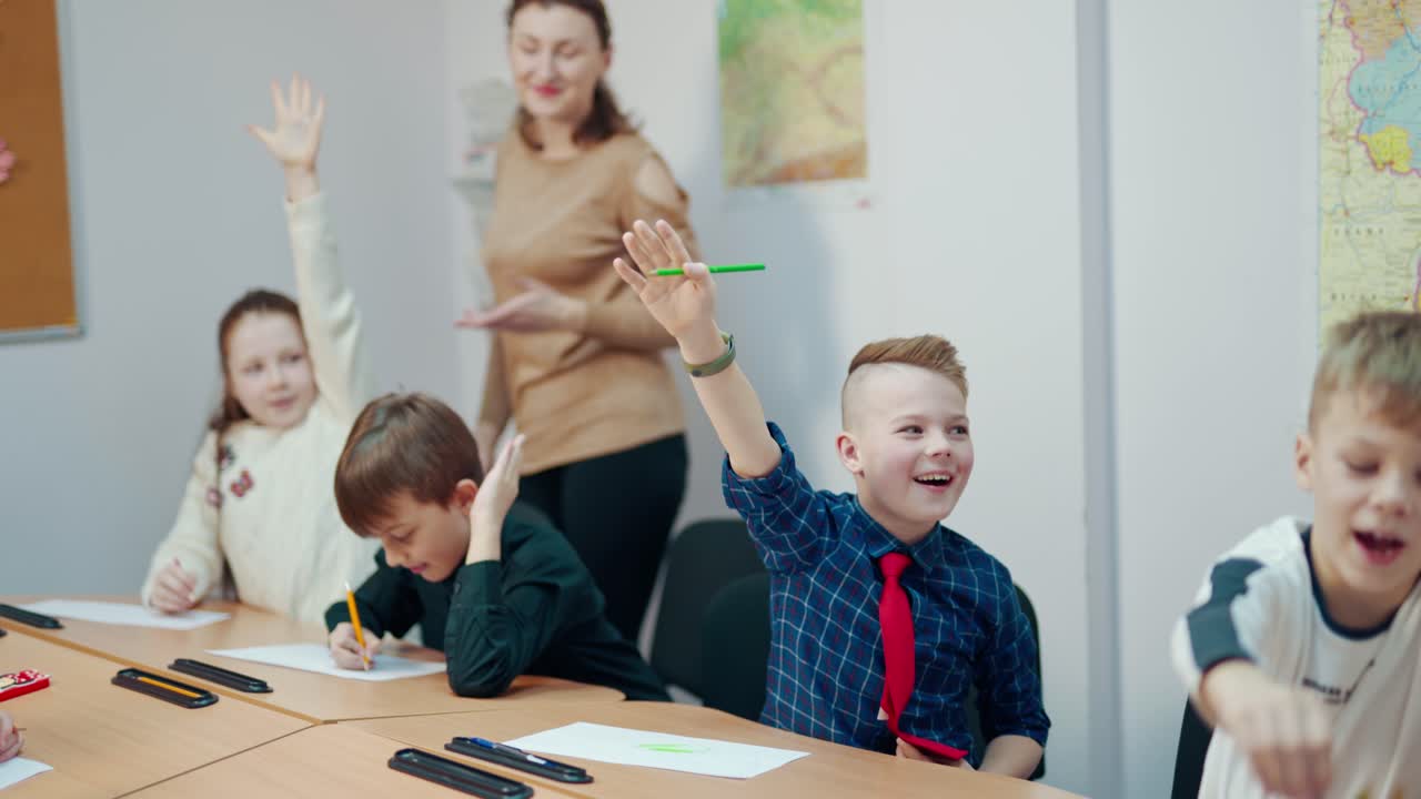 Back to school. Happy children sitting at desk together and raising their hands during the lesson. School teacher and cute little children at elementary school.