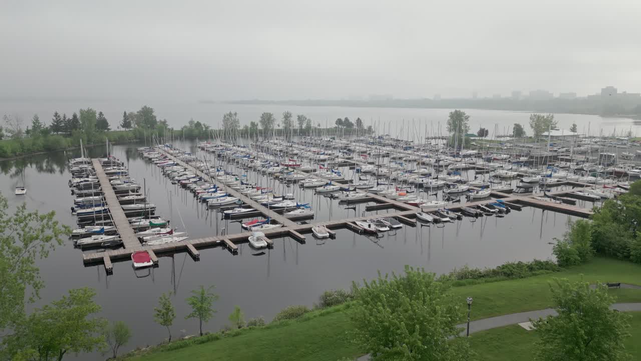 Marina in the early morning filled with sailboats moored in ultra calm water. Light cinematic fog. Aerial tracking upwards shot