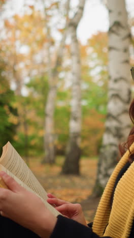mujer pensativa con gafas de sol, boina amarilla y bufanda a juego revisa un libro mientras está sentada en un paisaje de otoño, rodeada de hojas y árboles, disfruta de la reflexión tranquila y la literatura