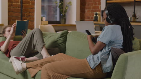 y chicas leyendo un libro y escuchando música con un smartphone en el sofá de casa
