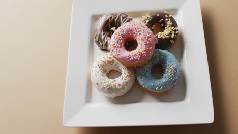 Video-of-donuts-with-icing-on-white-plate-over-pink-background