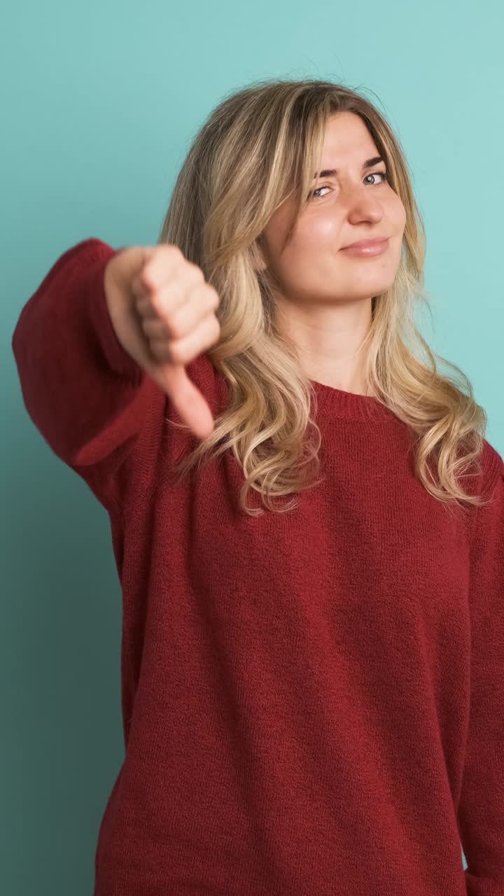 Sad young woman showing thumb down in blue studio