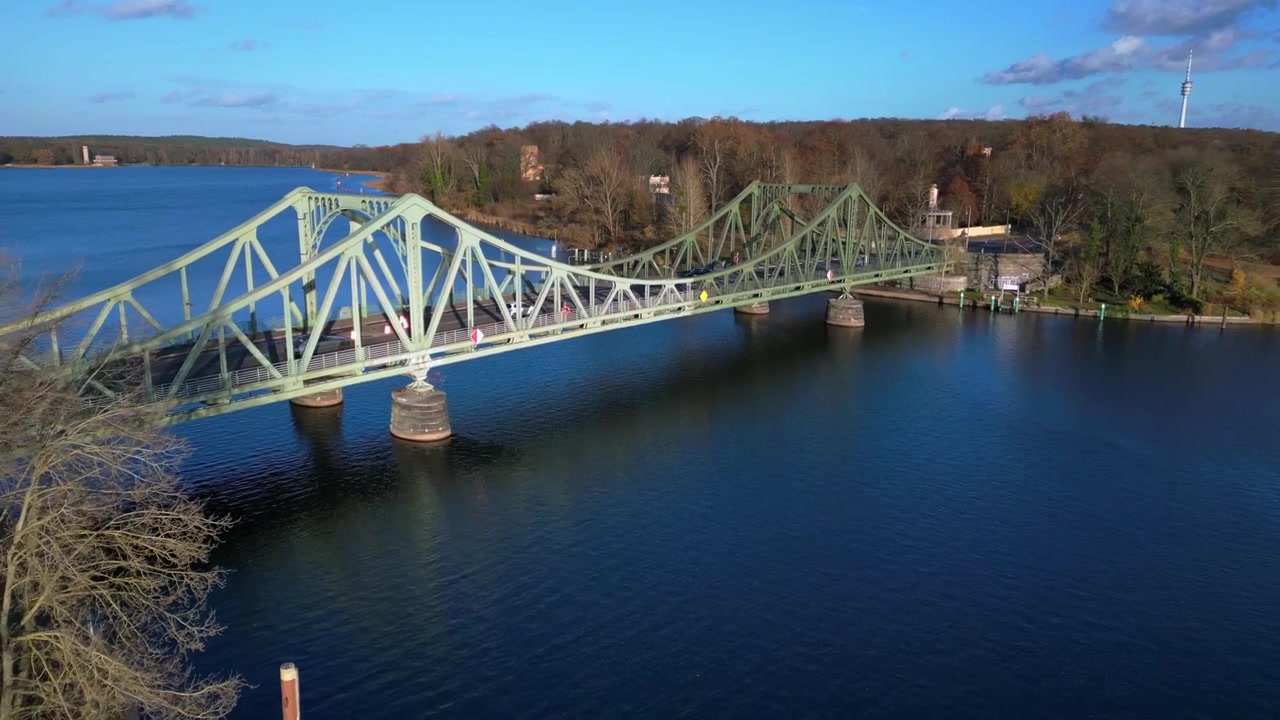 Ponte di Glienicke sul fiume Havel, con auto in transito durante un colorato tramonto autunnale. Volo drone inverso con vista aerea unica.