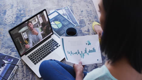 african american woman holding a document having a video call on laptop at home