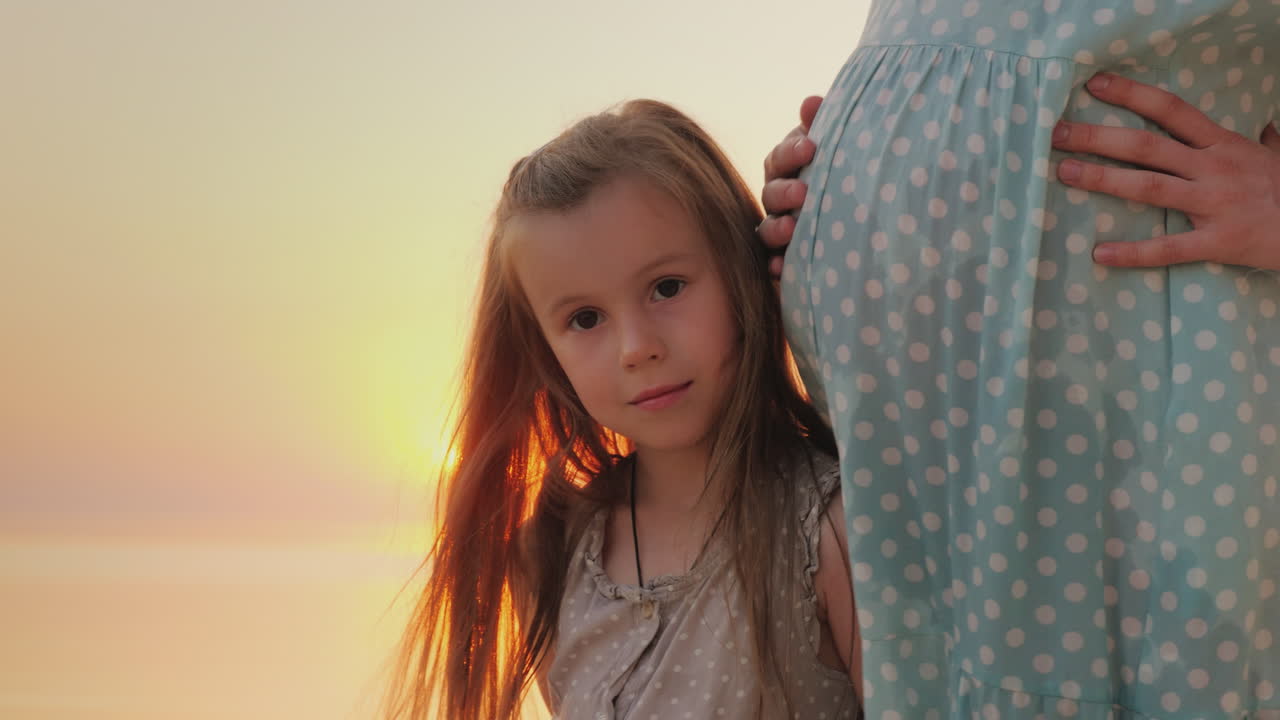 Ritratto di un bambino felice vicino a una madre incinta sullo sfondo del tramonto sul mare.