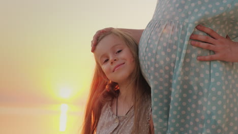 portrait of a happy child near a pregnant mother against the background of the sunset over the sea w