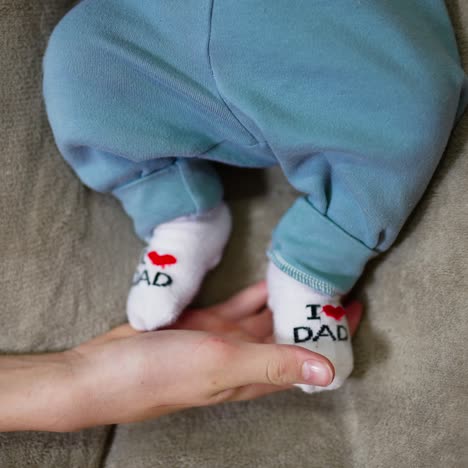 mother's hand holding small infant's feet. newborn kid's tiny feet in funny socks. close up