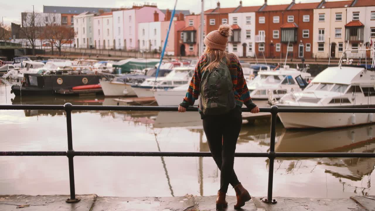 Plano aberto de uma mulher de pé no porto de Bristol, olhando para barcos.