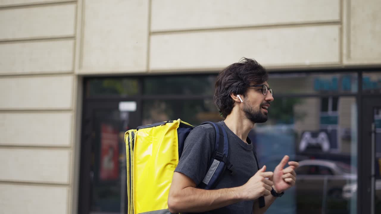 A bearded guy with a delivery backpack is fooling around, slow motion