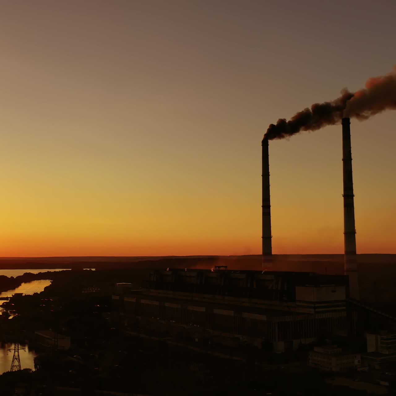 Harmful factory among nature at sunset. Dangerous smoke fills the air from industrial pipes. Manufacturing at dusk. Environment in danger. Global warming.