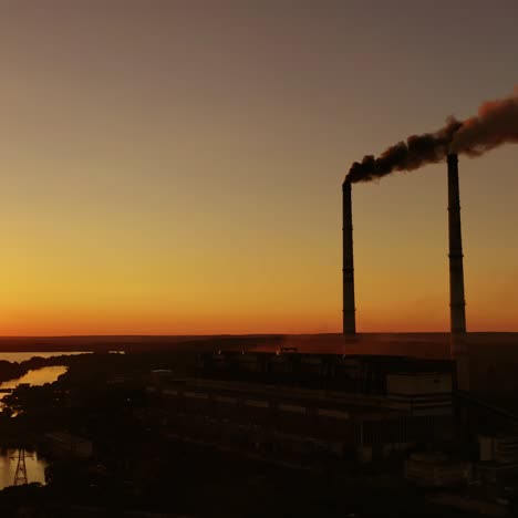 harmful factory among nature at sunset. dangerous smoke fills the air from industrial pipes. manufacturing at dusk. environment in danger. global warming.