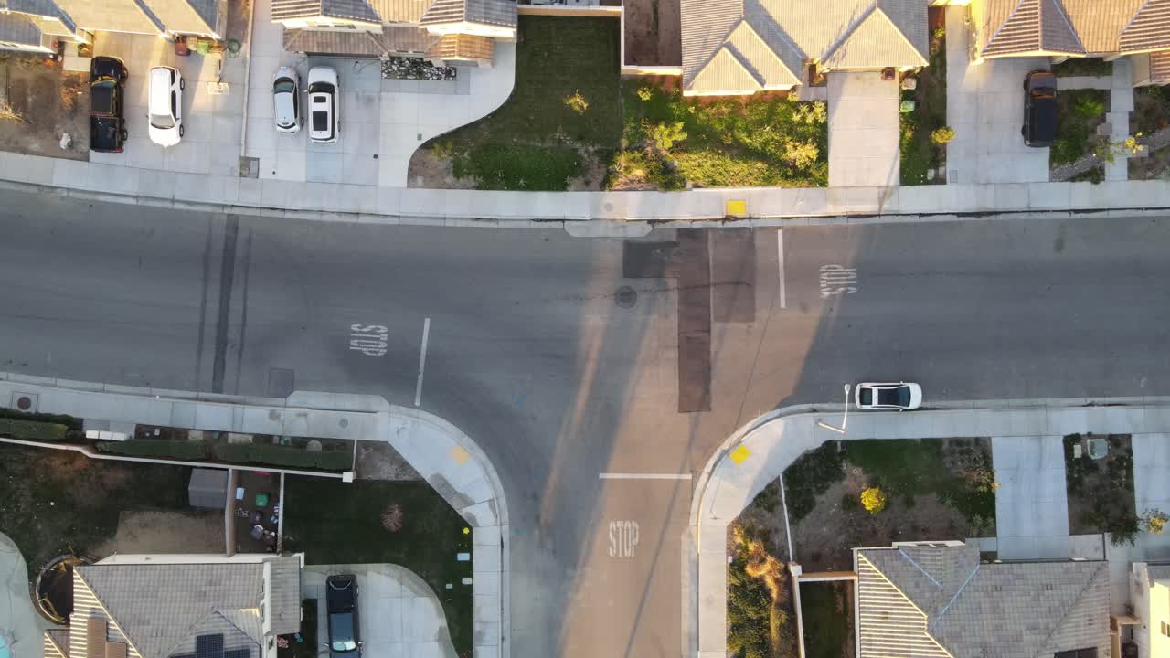 luz dorada baña un dron estático disparado sobre una tranquila intersección en forma de t en un vecindario del sur de california, con largas sombras anidadas entre los edificios