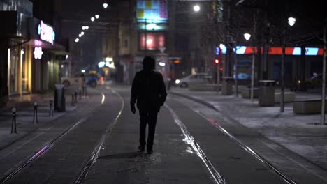 person walks in middle of empty side street on cold snowy night