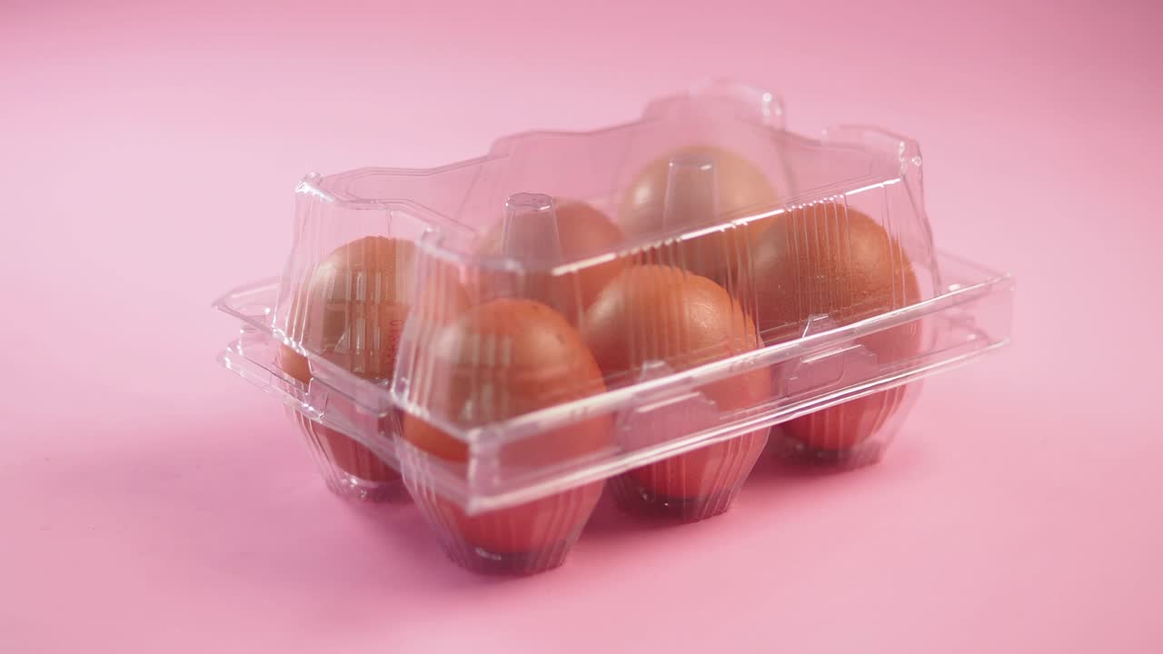 Sechs braune Eier in einem durchsichtigen Plastikkarton auf pinkem Hintergrund.