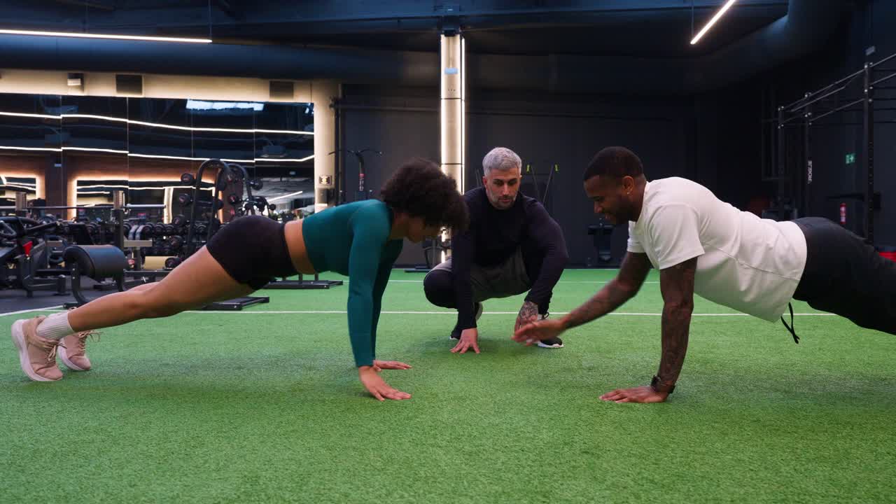 Mann und Frau machen Liegestütze mit Trainer in modernem Fitnessstudio