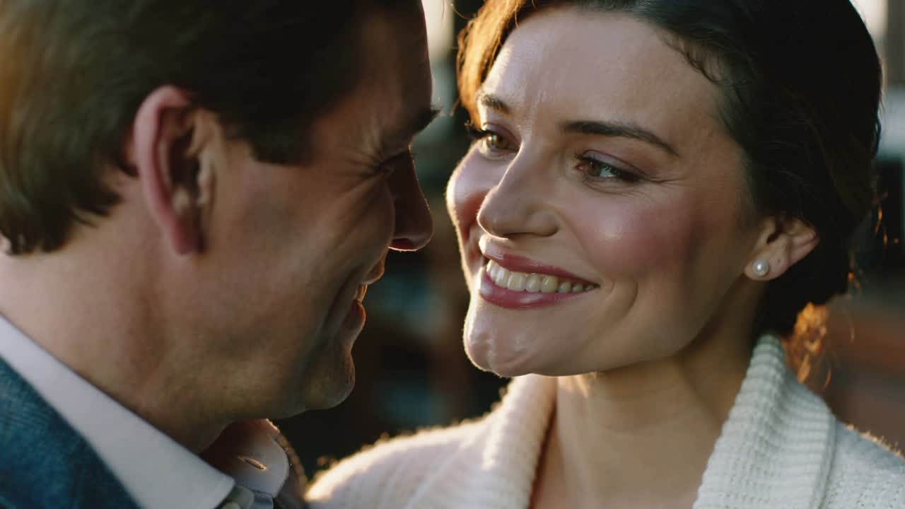 Close proximity spurring woman smiling and leaning toward man in blue jacket in lounge, pearl studs