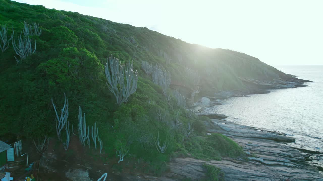 la órbita aérea nostálgica de un rayo de sol a través de una montaña con vegetación tropical y rocas con olas suaves, joao fernandes playa costa
