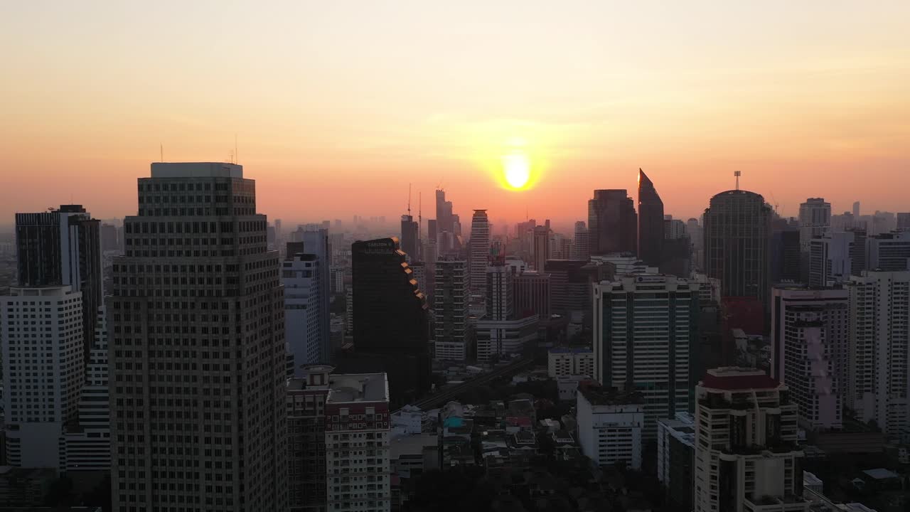 Vista aérea épica voando através de edifícios, horizonte e arranha-céus do distrito de Sukhumvit durante um nascer do sol vermelho e colorido em Bangkok, Tailândia