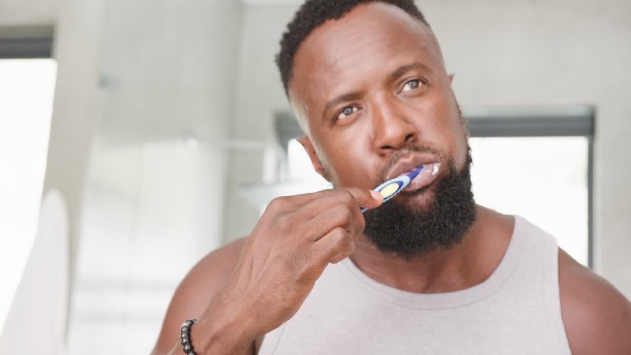 African American man checking mirror, lifting toothbrush and brushing teeth for hygiene in bathroom