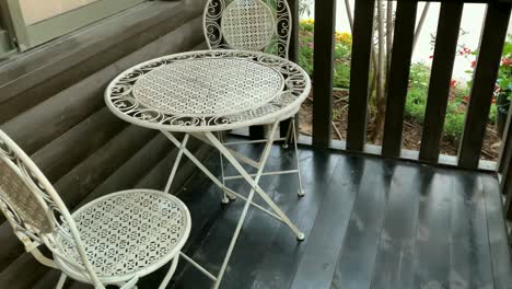 dos sillas de metal blanco y una pequeña mesa redonda en una terraza de madera marrón.