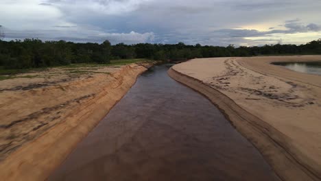 Clip-Aéreo-Siguiendo-Un-Arroyo-En-Una-Playa-De-Arena-Al-Atardecer