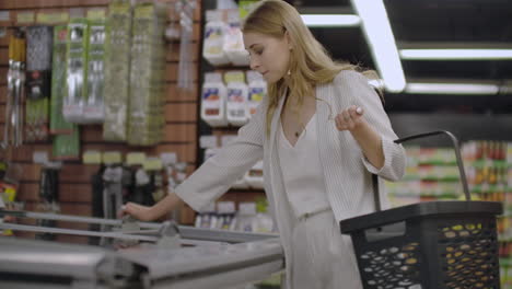 business woman in the supermarket takes out of the refrigerator frozen food reads the composition of the product and puts it in the basket.