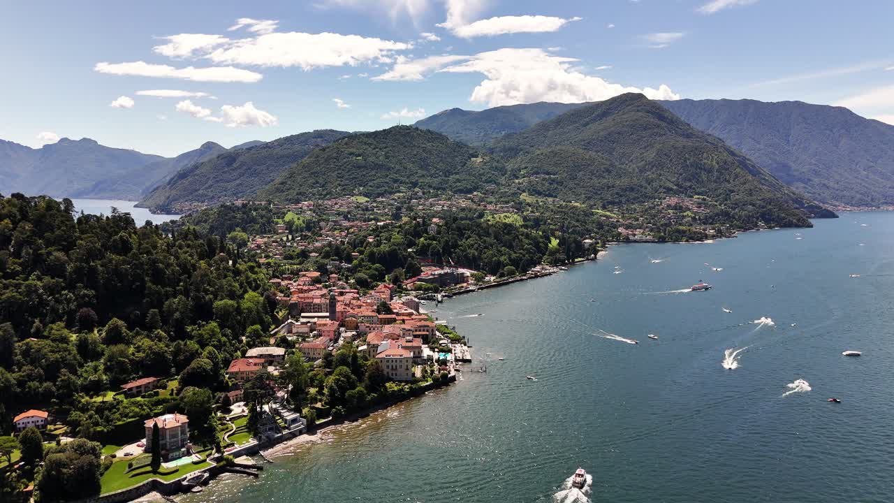 Aerial view of Bellagio on Lago di Como featuring the peninsula village, surrounding green mountains, vivid blue water and boats moving across the lake in bright summer weather conditions