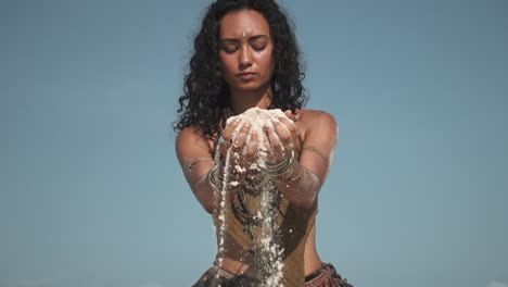 attractive eastern girl picking sand in palm and dissolve through fingers in slow motion