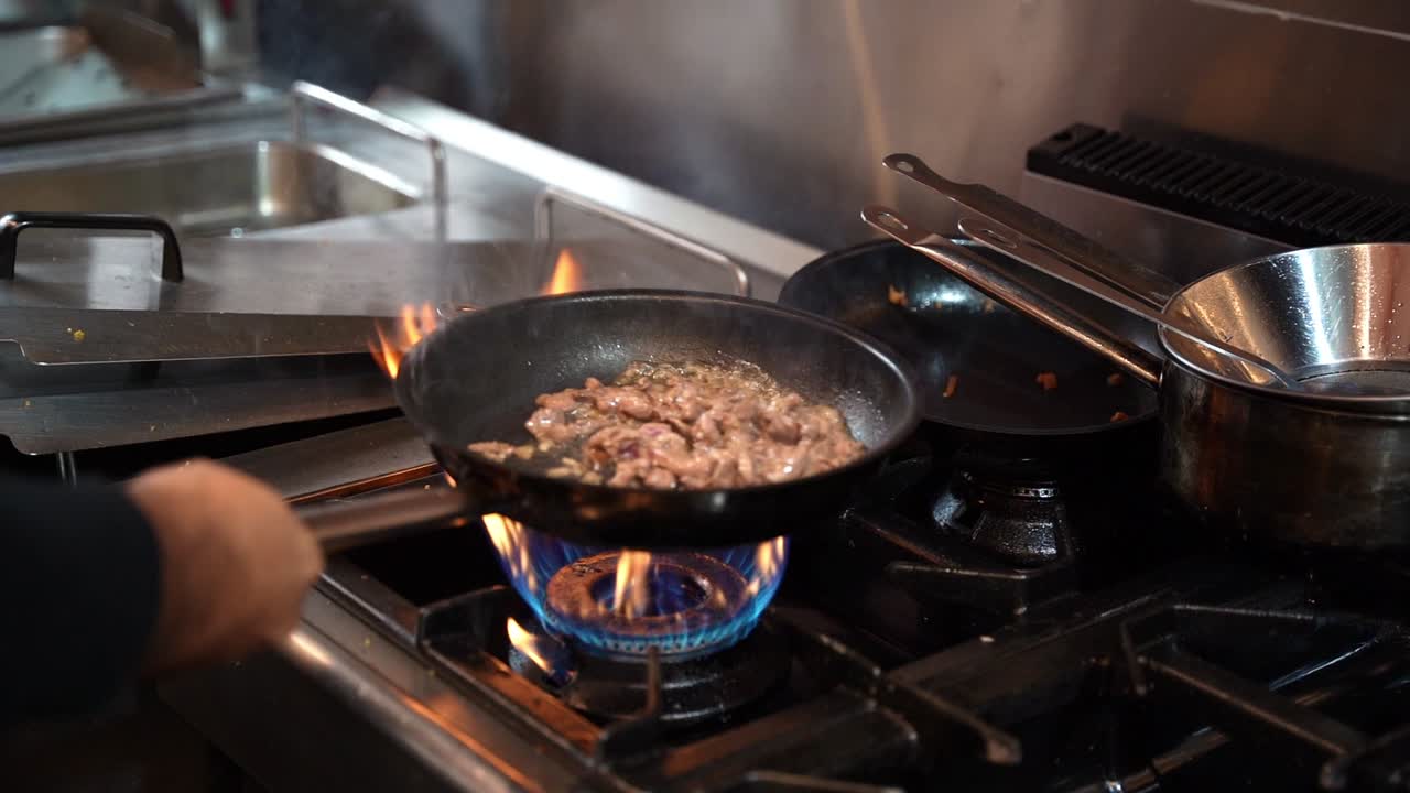 Chef stir-frying meat in a pan over an open gas flame with fire and smoke in a professional kitchen. Perfect for food, lifestyle, culinary, and restaurant projects