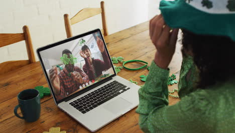 pareja sonriente y diversa que usa artículos en forma de trébol en una videollamada en una computadora portátil