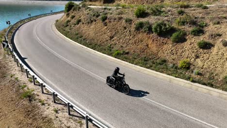 Biker-Passt-Das-Visier-An,-Während-Er-Auf-Einer-Landstraße-Mit-Blick-Auf-Den-Blauen-See-Fährt