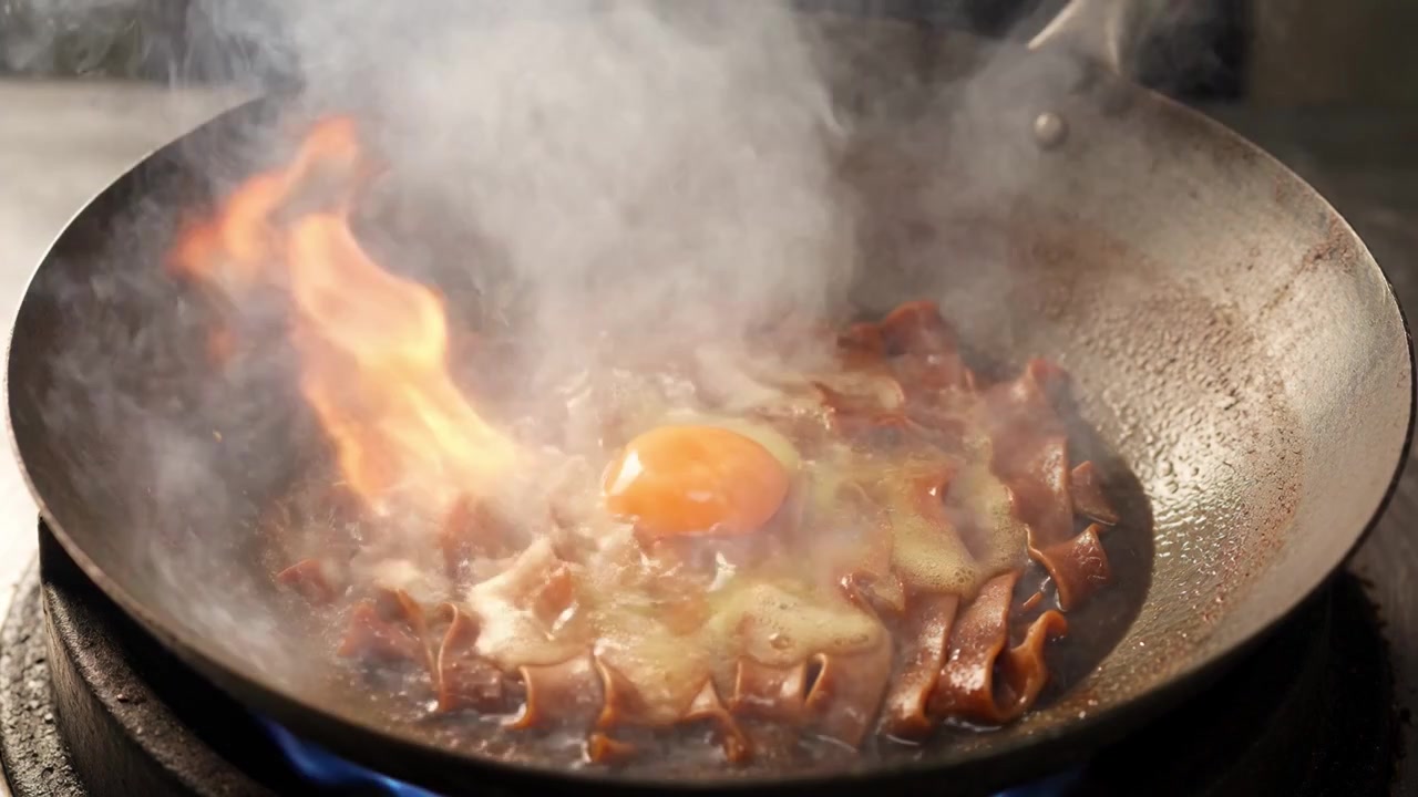 Chef che rompe un uovo in un wok con noodles sfrigolanti