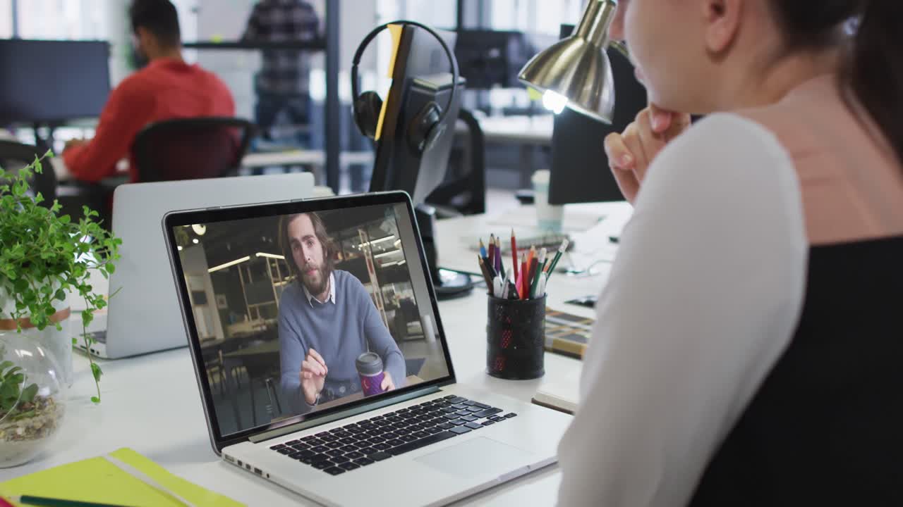 Caucasian woman having a video call on laptop with male colleague at office