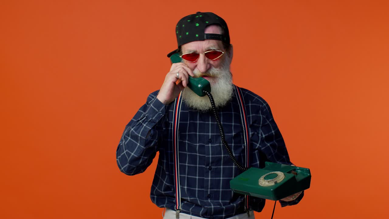 Crazy elderly bearded old man talking on wired vintage telephone of 80s, fooling, making silly faces