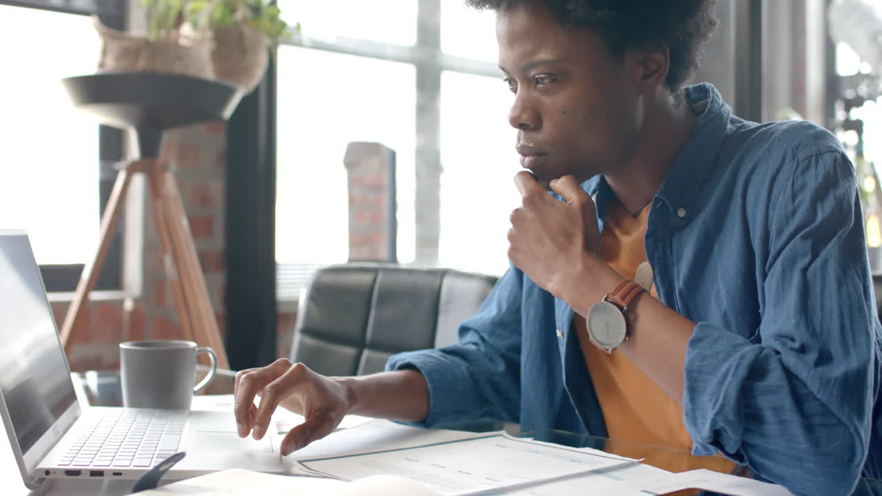 Focused african american casual businessman sitting at desk using laptop at home, slow motion