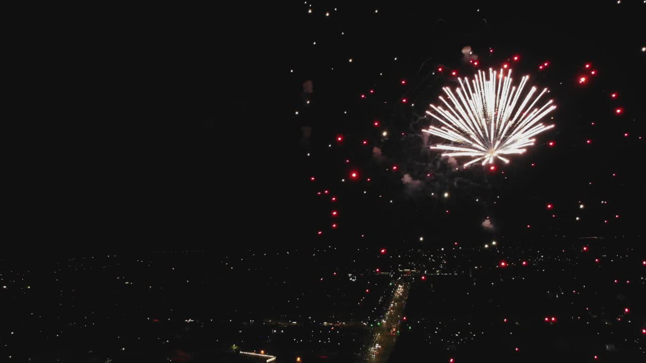 fuegos artificiales de colores en el cielo oscuro. disparo aéreo de fuegos artificiosos con luces de la ciudad en el fondo. luces nocturnas de la ciudad