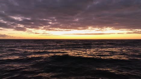 flight over wavey sea in orange sunrise with pink clouds and sunlight