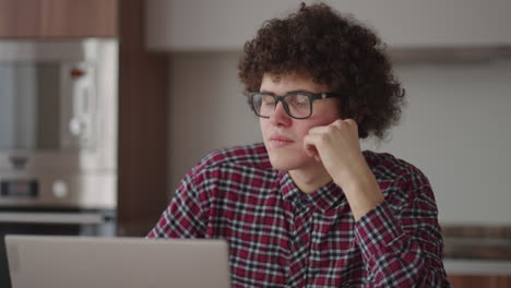 Brooding-serious-curly-freelancer-man-sit-at-table-in-comfortable-home-office-room-work-on-laptop-looks-concentrated-thinking-over-business-issue-solution-makes-telecommute-job