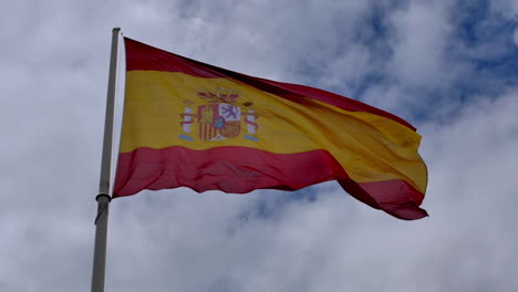 the spanish flag waves proudly against a moody sky, its red and yellow colors vibrant and alive, evoking strength, heritage, and national identity.