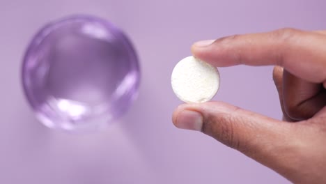 hand holding a pill over a glass of water