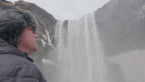 middle age man in warm winter clothes standing under skógafoss waterfall, natural landmark of iceland, close up