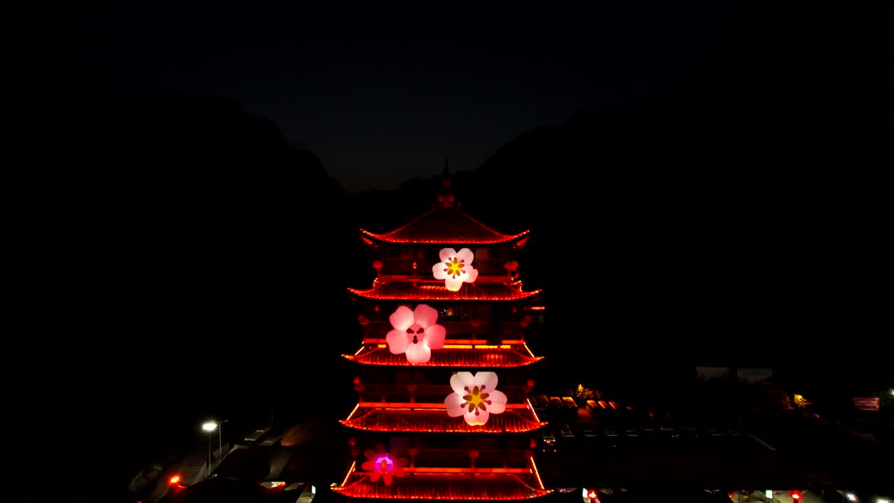 tomada aérea que revela la pagoda de la estación de boletos de wulingyuan iluminada por luces rojas con flores coloridas en el parque forestal nacional de zhangjiajie, china