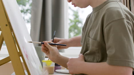 Closeup-of-girl-and-her-mom-using-paintbrushes-on-a-canvas