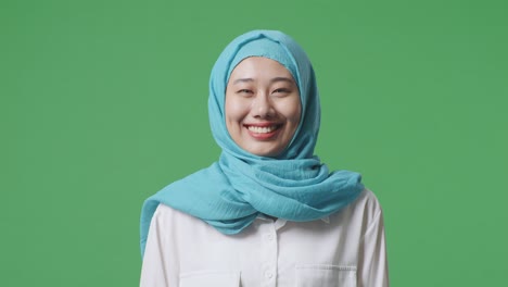 close up de una mujer musulmana asiática mirando a la cámara y sonriendo mientras está de pie en el estudio de fondo de la pantalla verde