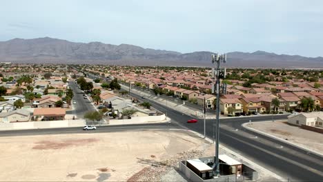 cell tower on the foreground in a las vegas suburb with mountains beyond the valley - ascending aerial view